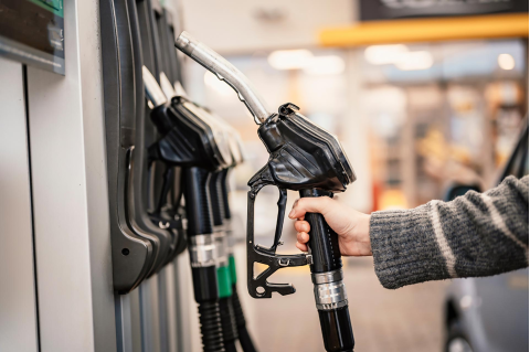 A hand reaching for a gasoline pump at a gas station