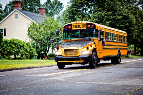 A yellow school bus driving down a suburban street. A Tufts study finds that the METCO school desegregation program in Boston benefits urban K-12 students in test scores, attendance rates, and college outcomes