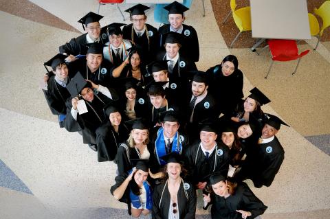 Overhead group photo of graduating Film and Media Studies students in caps and gowns smiling and posing together during commencement celebrations