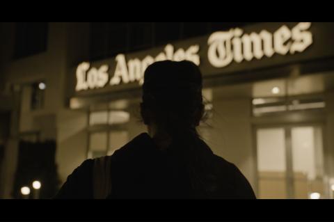 Silhouetted figure standing at night in front of the illuminated Los Angeles Times building