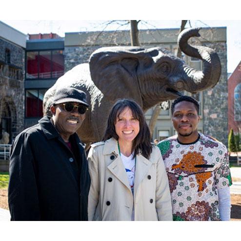 Three people standing in front of statue of Jumbo the elephant in front of Barnum Hall on Tufts’ Medford campus