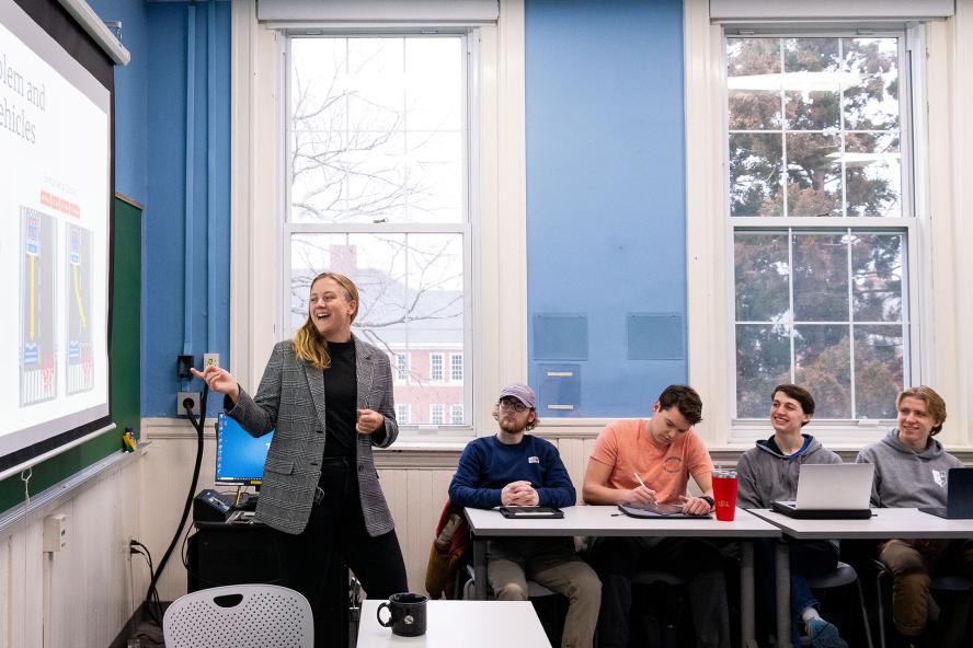 Professor teaching in a classroom with students listening and presentation displayed on a pulldown screen