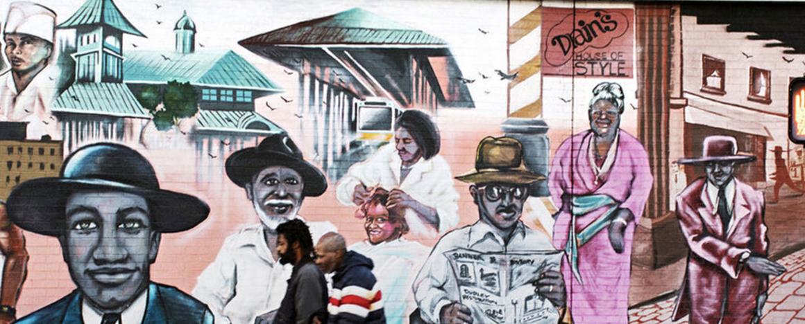 Two men walking down a street with a historical black history mural behind them