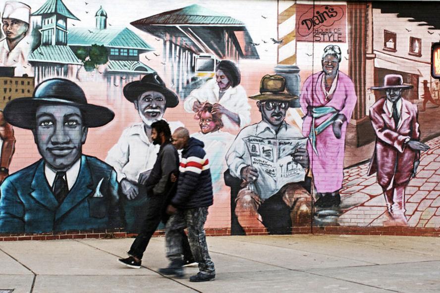 Two men walking down a street with a historical black history mural behind them