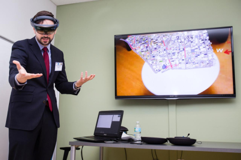 A man with a VR headset on gestures and talks to an audience. Researchers at Tufts’ high-tech brain center are working to save lives of soldiers and first responders by learning how their minds work under pressure