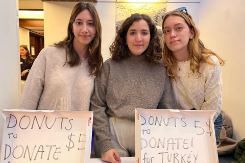 Three woman stand behind a table where they are accepting donations for earthquake relief. 