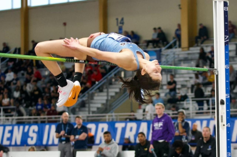 Jaidyn Appel doing a high jump, crossing over the bars as people look on from the stands. Jaidyn Appel, A23, takes the NCAA title for high jump for the second year in a row, and Tufts takes seventh place team finish 