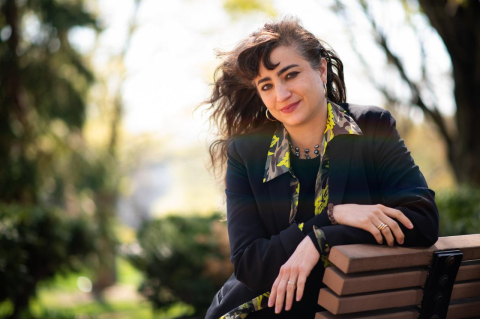 Sara Deniz Akant with arms resting on the back of a park bench, looking toward the camera. Poetry connects us to ourselves and others on a fundamental level, says the professor of the practice of poetry at Tufts. 