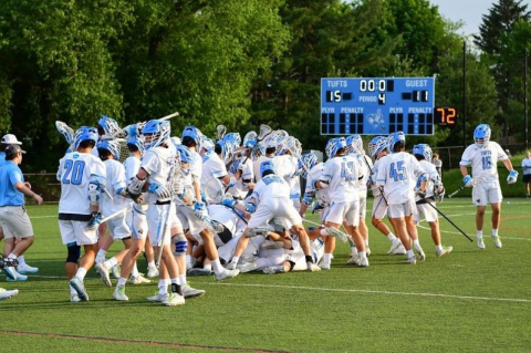 A large group of Tufts men’s lacrosse players crowds together in the field to celebrate their victory. 