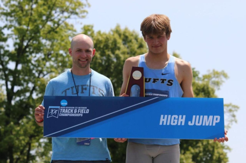 Two men standing at a podium, one holding a trophy. A Tufts high jumper wins national top spot for NCAA Division III, while men’s lacrosse is NCAA national runners up and women’s rowing places third in nationals 