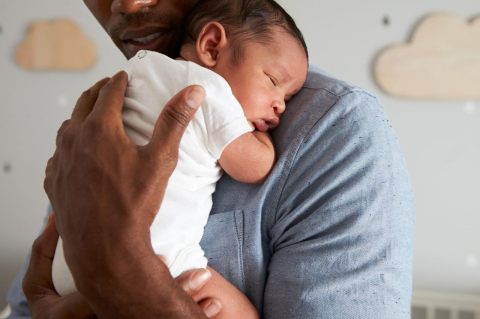 A father holds his infant son in the baby&#039;s nursery