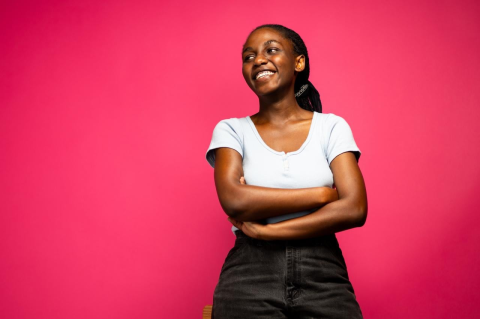 Noella Akuzwe, smiling, stands in front of a pink background.