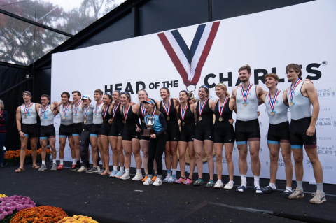 18 students in rowing outfits line up with trophies. The Tufts men’s and women’s first varsity teams take the Collegiate Eights at the Head of the Charles Regatta
