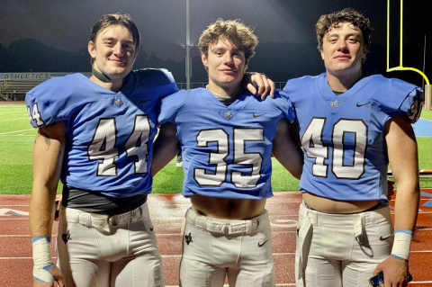 Three football players lined up outside after a game, wearing Tufts football uniforms. Five sets of brothers, including triplets, are on the gridiron on Saturdays for the Jumbos