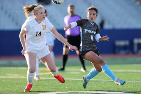 Two women’s soccer players from opposing teams vie for the ball, while a referee looks on. The Tufts women’s soccer team advanced to the 2023 NCAA semifinals on penalty kicks.