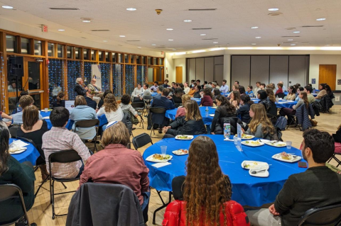 Two men seated in front of a large crowd around tables. A new series hosted by Tufts Hillel this spring seeks to bring critical thinking and civil discussion to bear on current events