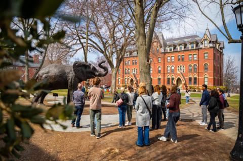Prospective students and their families gather around a Jumbo the elephant statue on the Tufts campus. The students admitted to the Tufts undergraduate Class of 2028 are described as civic-minded, entrepreneurial, and committed to collaboration.