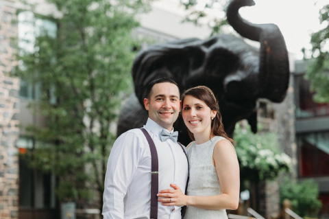 A man and woman in formal attire in front of the Jumbo statue on the Tufts University campus.