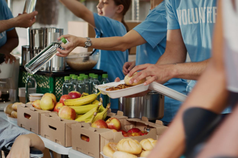 A group of people in blue T shirts that say “volunteer” hand out food items from behind a table.
