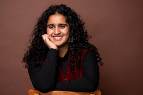 A woman smiles while resting her chin on her hand