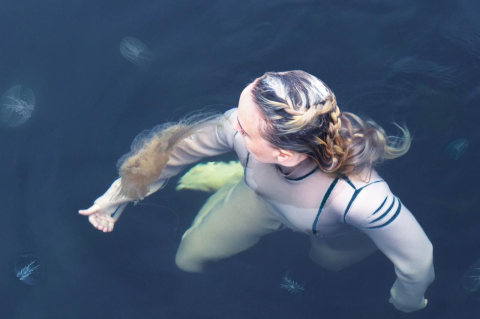 A woman in costume interacts with sea creatures in the ocean