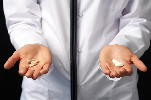 A person wearing a medical white coat holds out their two open hands, each with different pills 