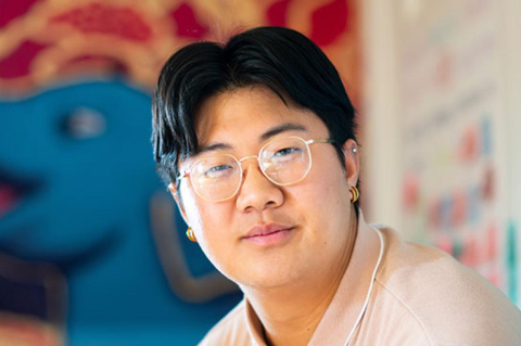 a male student with a glasses sitting in front of a large elephant poster