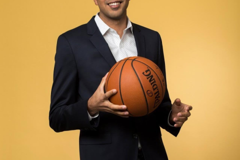 Gautam Kapur wears a black suit and white shirt while holding a basketball with his right hand.